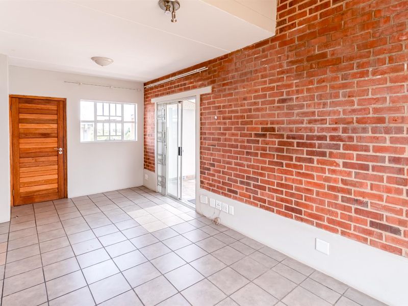 An empty living room featuring an exposed brick feature wall, tiled flooring, and a sliding glass door providing access to the exterior.