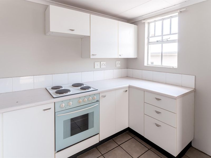 A functional, empty kitchen featuring white built-in cabinetry, a tiled backsplash, laminate countertops, and a built-in electric stove and oven.