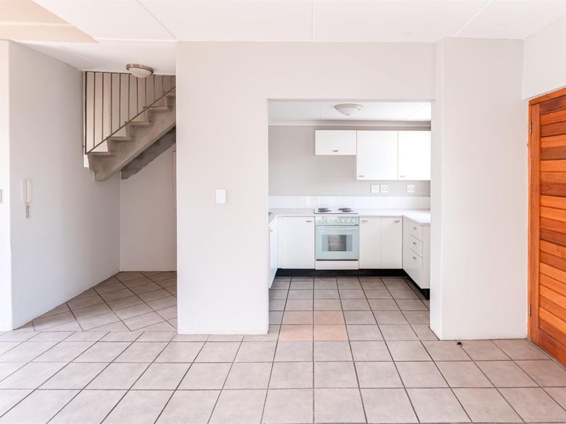 Open plan living area featuring tiled floors, a functional kitchen with built-in cabinetry and stove, and an internal staircase.