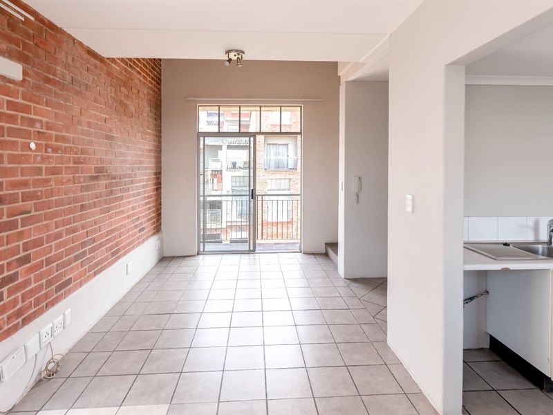 Open plan living area featuring an exposed brick feature wall, tiled flooring, and direct access to a balcony, adjacent to a functional kitchen space.