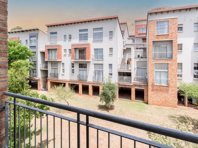 View of the apartment complex rear elevation featuring brick and plaster facade, metal balcony railings, and ground-level covered parking bays.