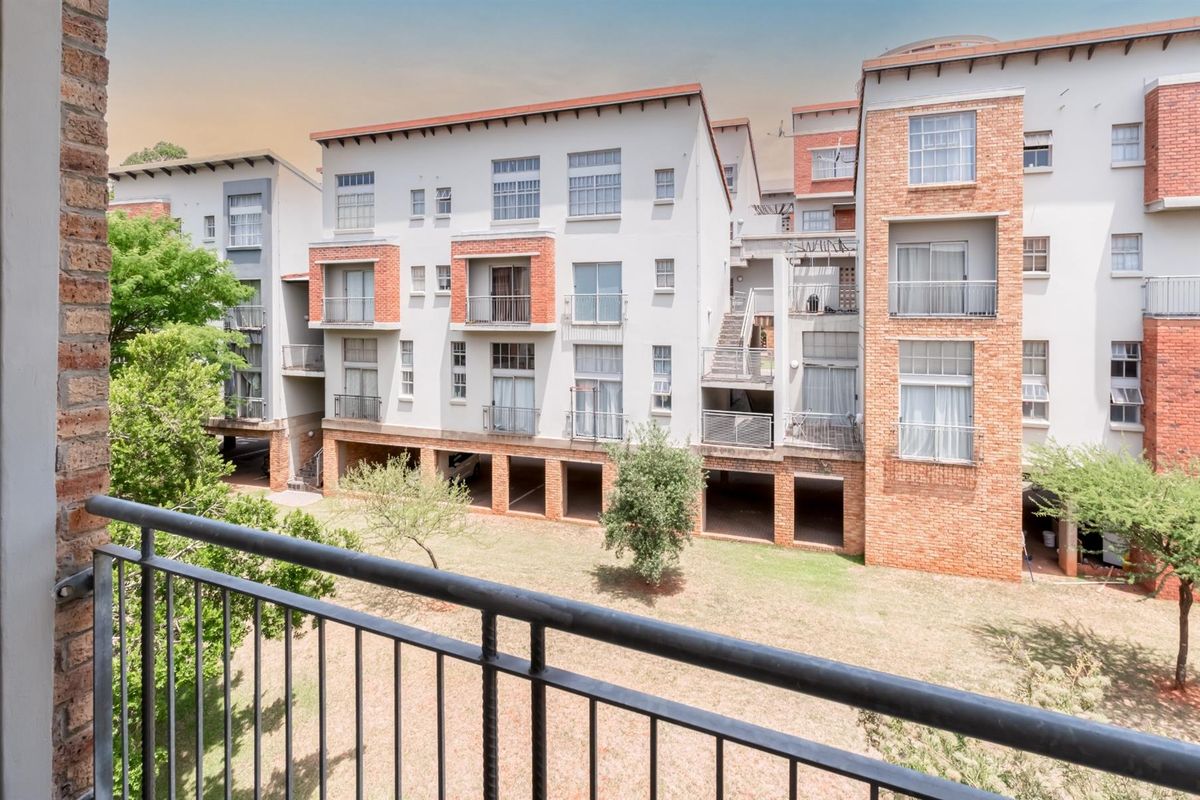 View of the apartment complex rear elevation featuring brick and plaster facade, metal balcony railings, and ground-level covered parking bays.