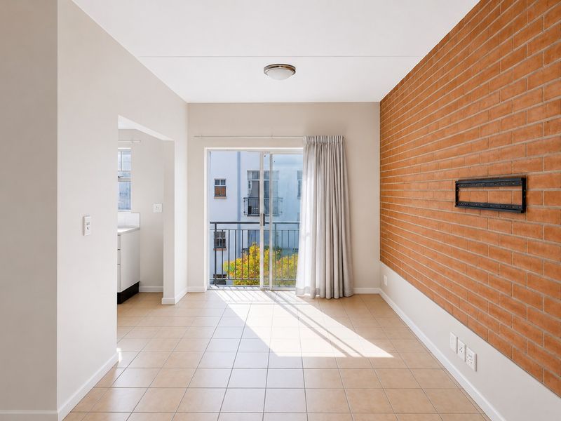 Bright, empty living area featuring a distinctive exposed brick wall, ceramic tiled flooring, and direct access to a balcony through sliding glass doors.