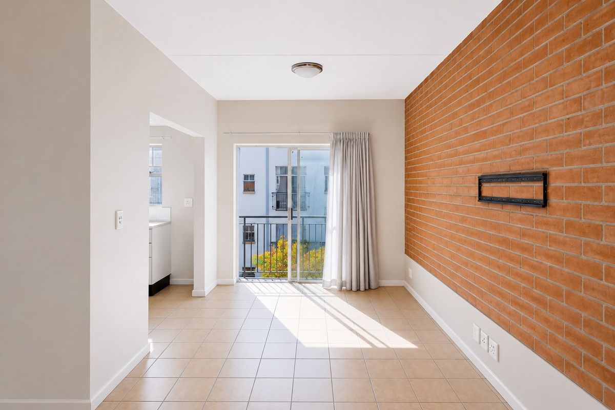 Bright, empty living area featuring a distinctive exposed brick wall, ceramic tiled flooring, and direct access to a balcony through sliding glass doors.