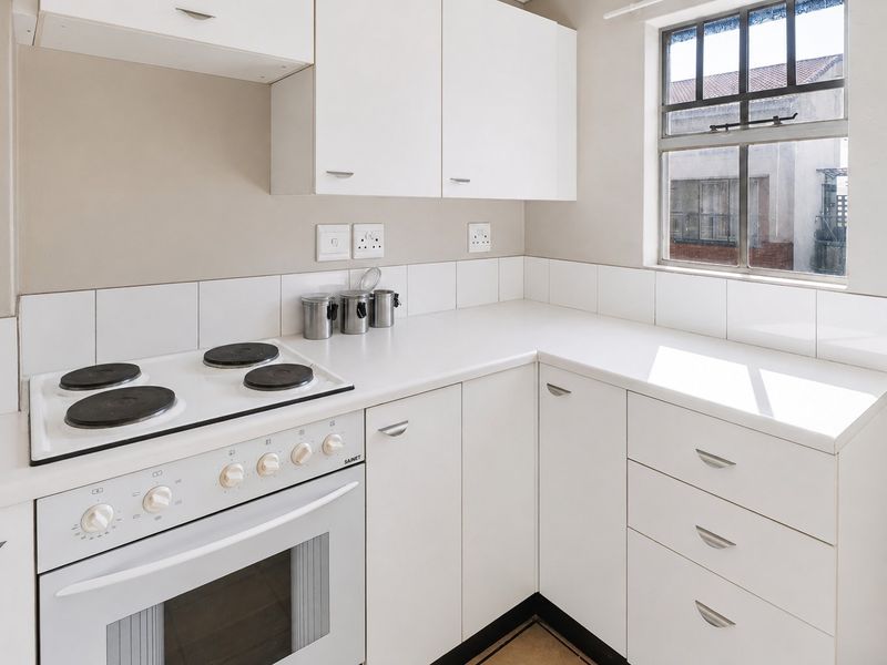 A clean, functional kitchen featuring white built-in cabinetry, a white electric stove with oven, and a tiled backsplash under a steel-framed window.