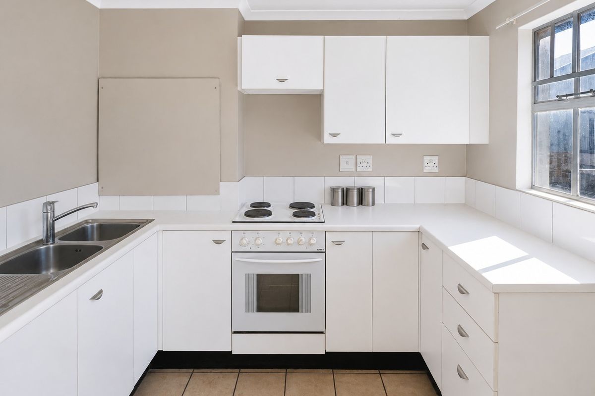 A clean, functional kitchen featuring white cabinetry, a stainless steel double sink, an electric hob and oven, and neutral tiled flooring.