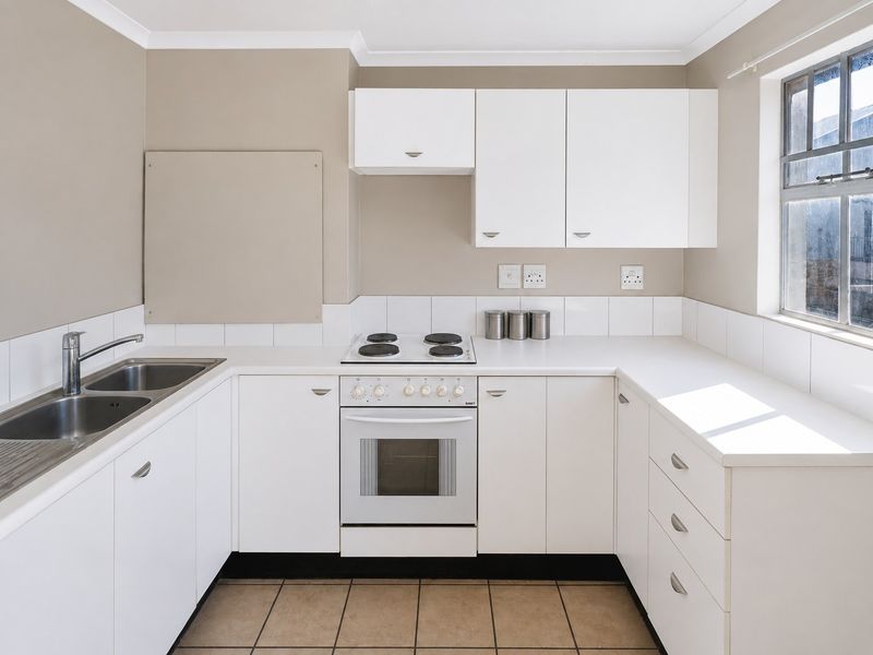 A clean, functional kitchen featuring white cabinetry, a stainless steel double sink, an electric hob and oven, and neutral tiled flooring.