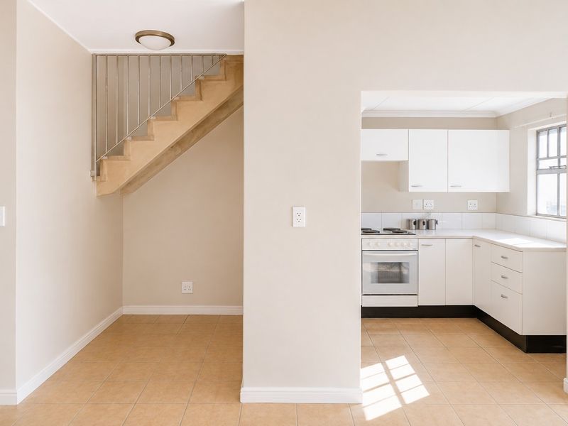 Open plan living area featuring a staircase with metal balustrade and a separate kitchen with white cabinetry, gas hob, and oven.