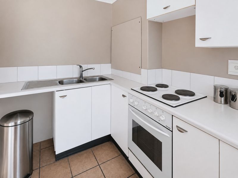A functional kitchen featuring white cabinetry, laminate countertops, a double basin sink, and a built-in electric stove and oven with tiled backsplash.