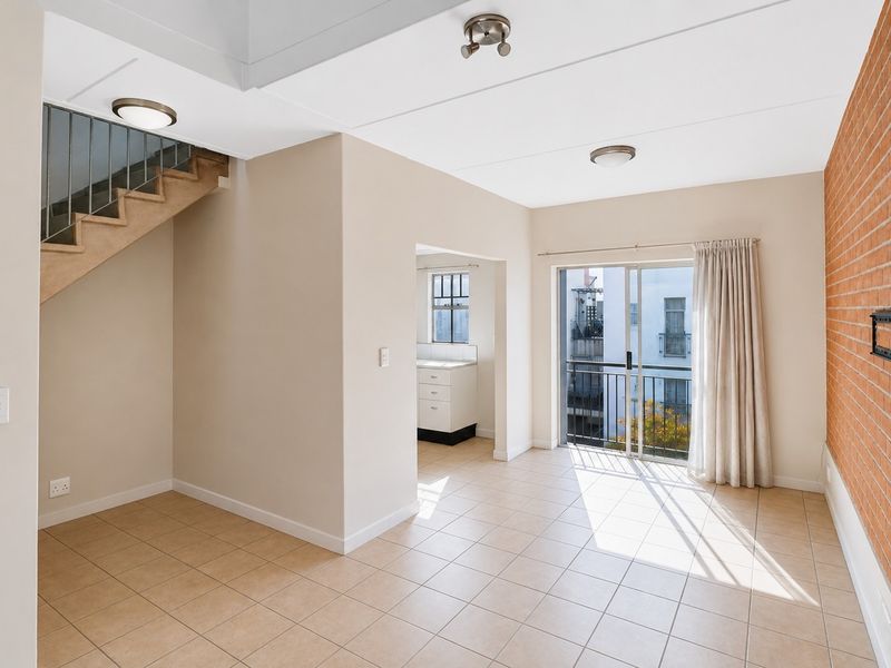 Spacious living area featuring an exposed brick feature wall, tiled flooring, and direct access to a balcony through sliding glass doors.