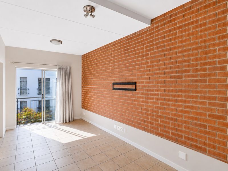 Bright living area featuring an exposed brick feature wall, tiled flooring, and a sliding glass door leading to a balcony.