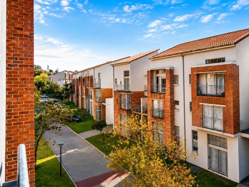 Exterior view of a multi-story apartment complex featuring brick and plaster facades, private balconies, and well-maintained communal gardens and paved driveways.