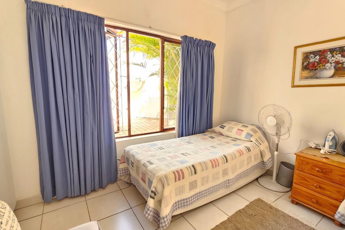 A functional bedroom featuring tiled flooring and a window with security gate, providing natural light and access to the exterior.