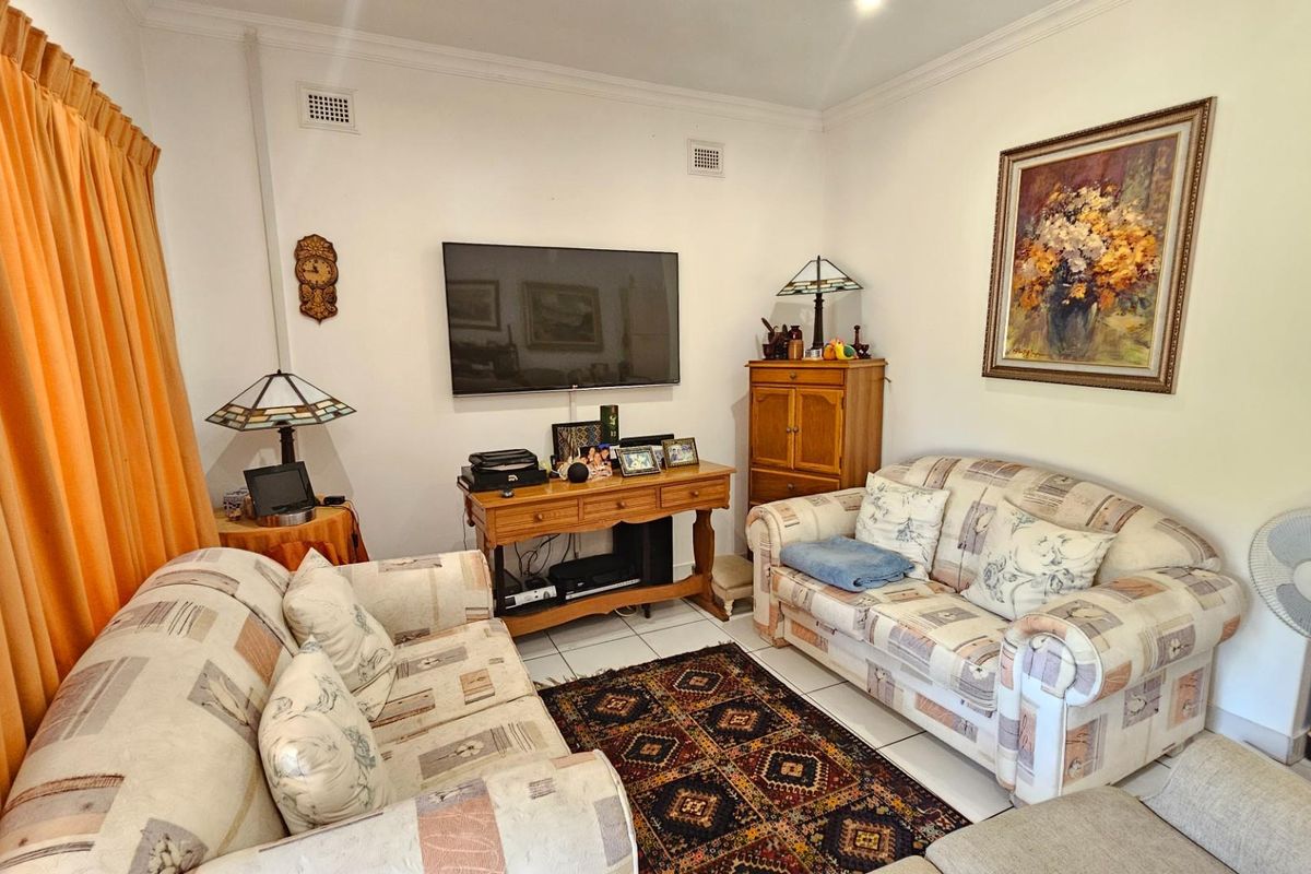 A comfortable living room featuring tiled flooring, wall-mounted television, and classic ceiling cornices, offering a functional space for relaxation.