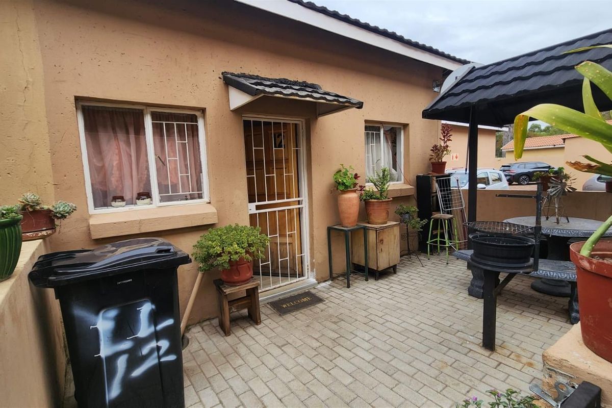 A paved rear patio area featuring a small covered entrance, security gate, and built-in structural elements, providing a functional outdoor space.