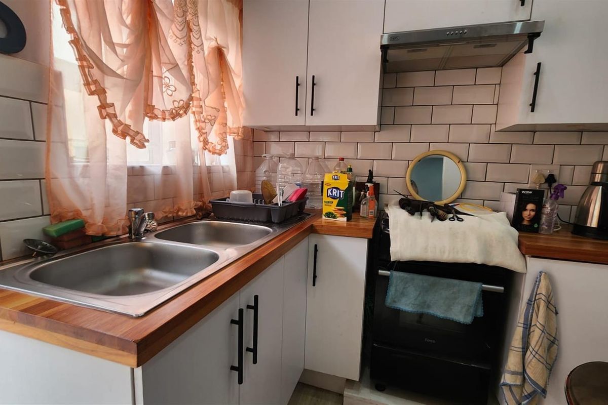 Compact kitchen featuring white cabinetry, subway tile backsplash, wooden countertops, and a double stainless steel sink with an integrated oven and extractor fan.