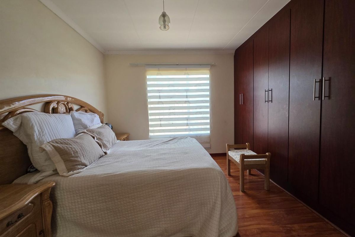 A well-maintained bedroom featuring dark wood built-in cupboards, laminate flooring, and a window fitted with a modern zebra blind.