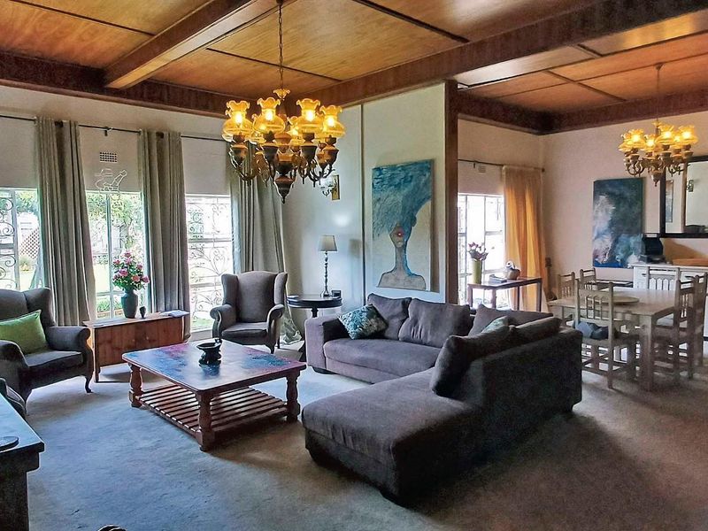 Spacious open-plan living and dining area featuring high timber-beamed ceilings, large windows with security gates, and classic chandelier lighting.
