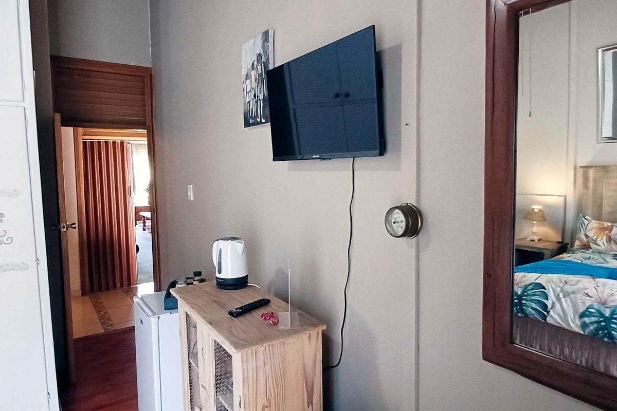 A bedroom featuring built-in wardrobe storage, a wall-mounted television, and a large mirror, with direct access to an adjoining room.