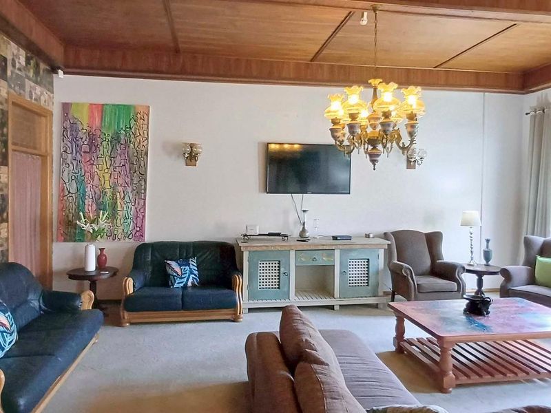 Spacious living room featuring a high timber-paneled ceiling, decorative chandelier, and wall sconces, offering a warm and traditional aesthetic.