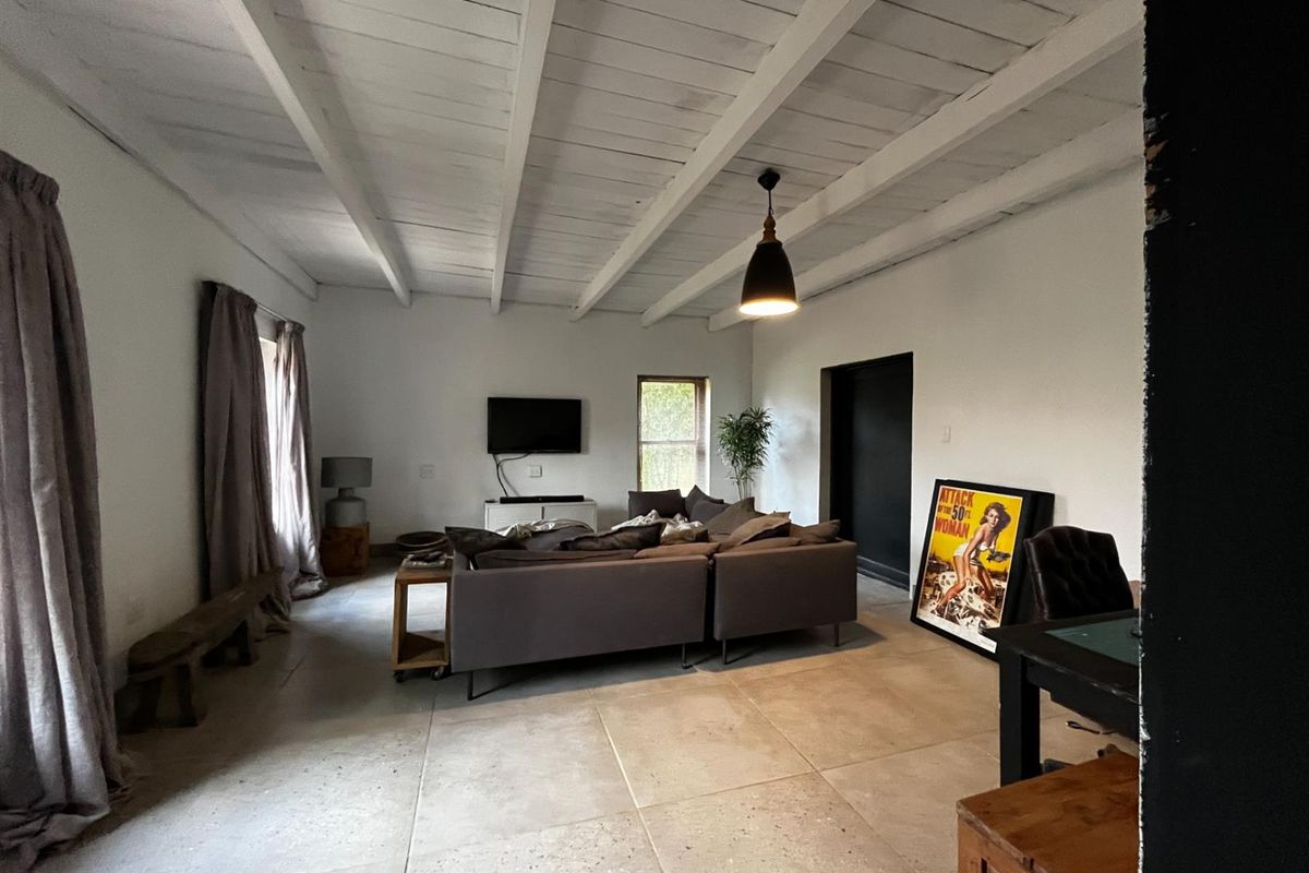 Spacious living room featuring exposed white timber beam ceilings, large format floor tiles, and a neutral aesthetic with ample natural light.