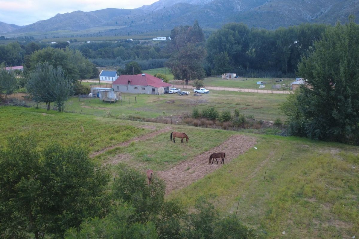 An aerial view of a rural property featuring expansive pasture land, fencing, and mountain vistas in the background.