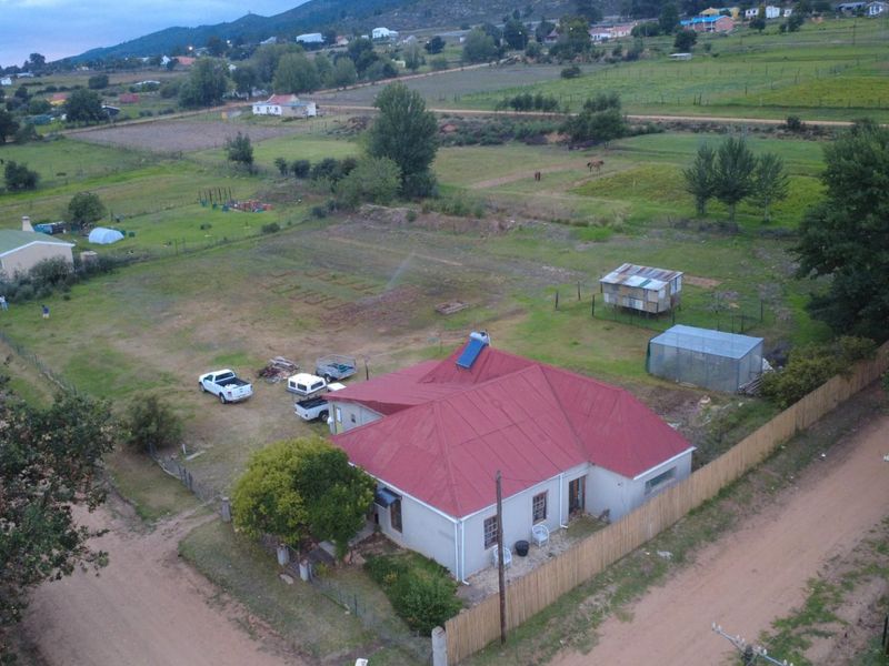 Aerial view of a residential property featuring a large plot of land, a house with a red metal roof, and perimeter fencing.