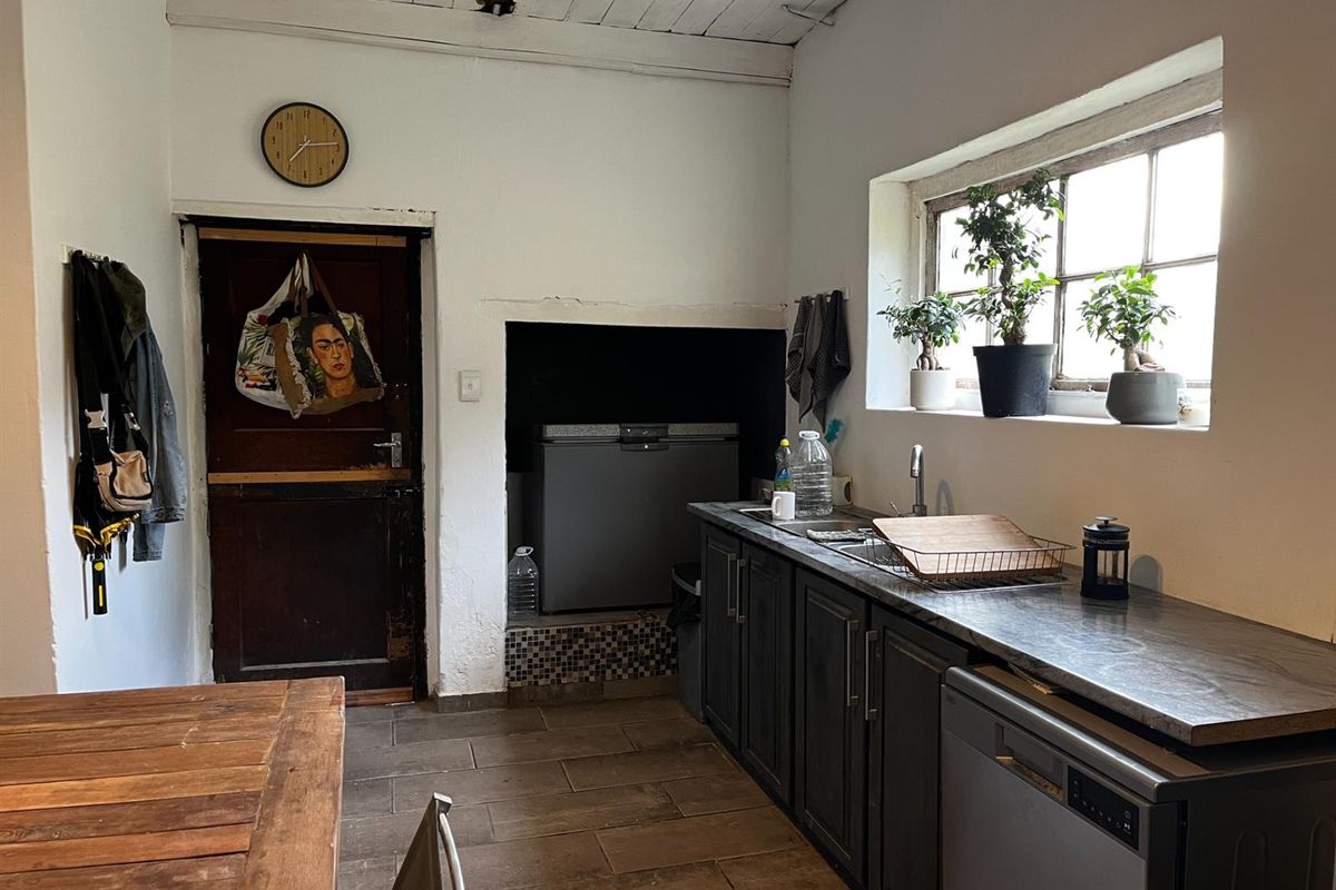 A functional kitchen area featuring dark cabinetry, a stainless steel sink, tiled flooring, and a rustic timber ceiling with a built-in alcove.