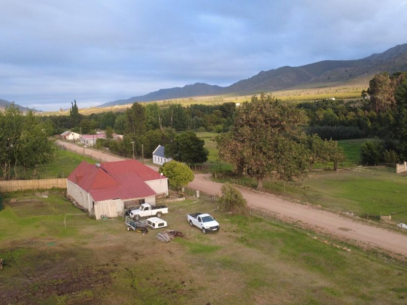 Aerial view of a rural property featuring a house with a red metal roof, surrounded by open land and mountain scenery.