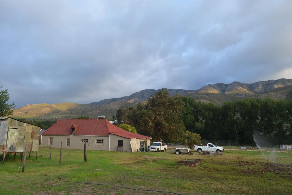 A rural property featuring a house with a red metal roof, an adjacent outbuilding, and expansive mountain views in a natural setting.
