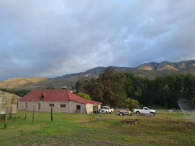 A rural property featuring a house with a red metal roof, an adjacent outbuilding, and expansive mountain views in a natural setting.