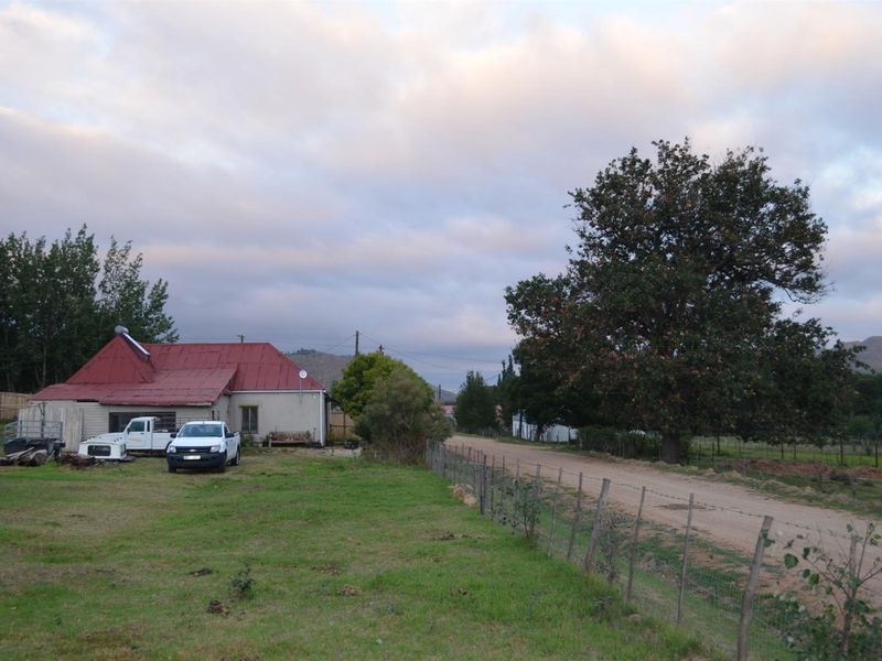 A rural property featuring a single-story house with a red corrugated metal roof, solar water heater, and expansive surrounding grounds.