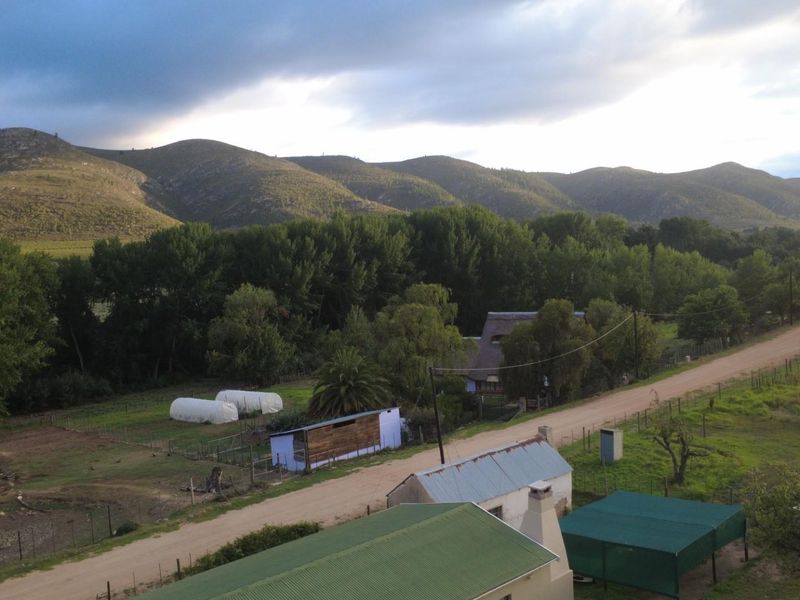 An aerial view of a rural property featuring outbuildings, a dirt road, and expansive mountain landscape views.