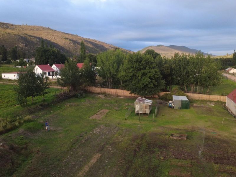 An aerial view of the property grounds featuring open land, perimeter fencing, and existing outbuildings set against a scenic mountain landscape.
