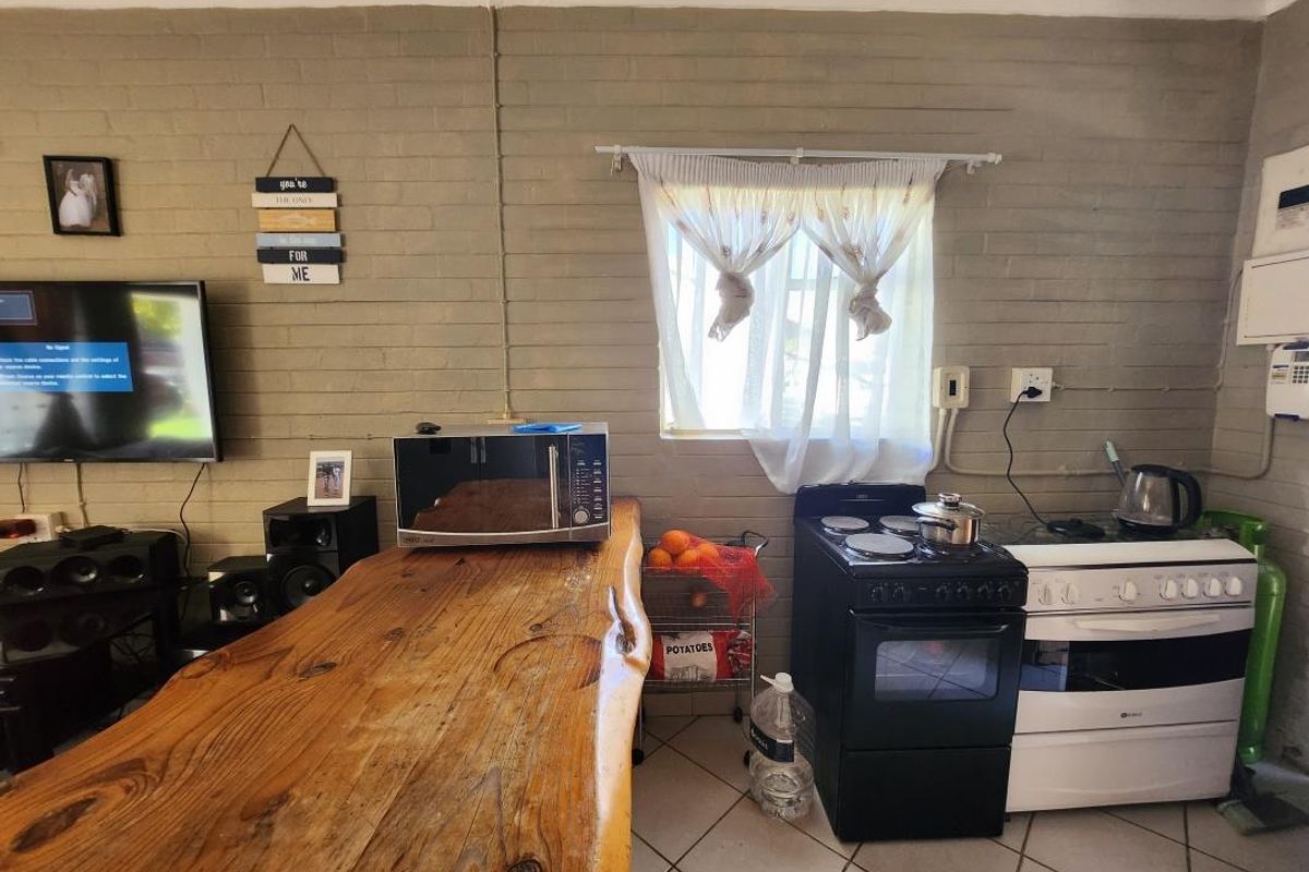 A compact kitchen area featuring exposed brick walls, tiled flooring, and a freestanding stove, offering potential for modernization and improved layout efficiency.