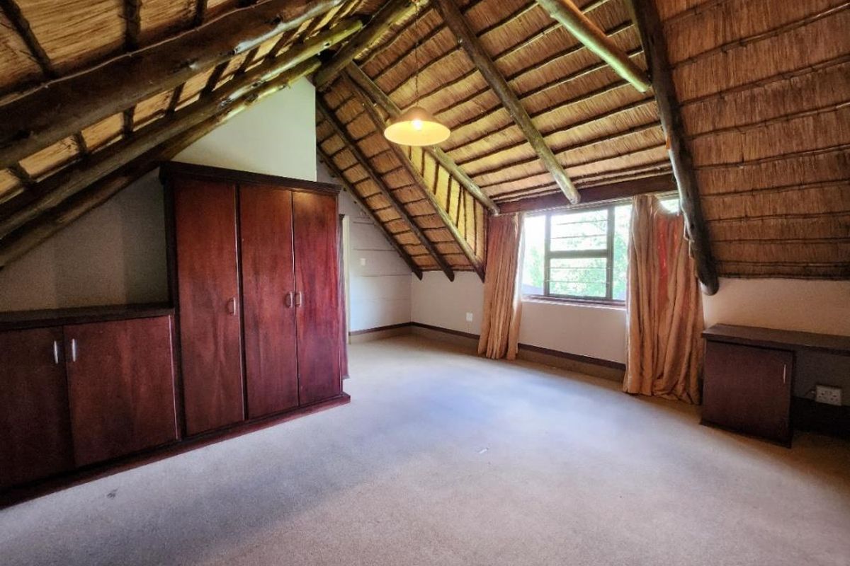 Spacious bedroom featuring a unique vaulted thatched roof with exposed timber rafters, built-in wooden cabinetry, and a built-in desk area.