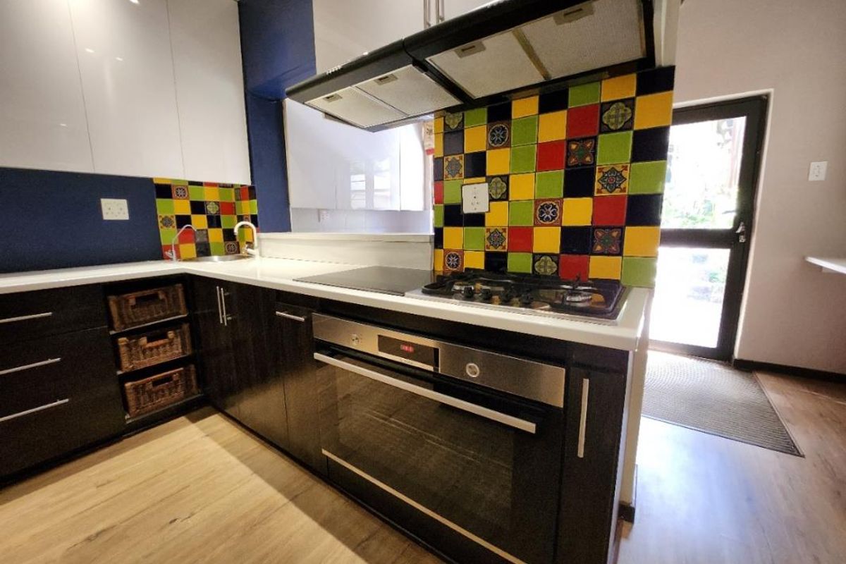 Modern kitchen featuring high-gloss cabinetry, a built-in oven with gas hob, extractor fan, and a vibrant multi-colored tiled splashback.