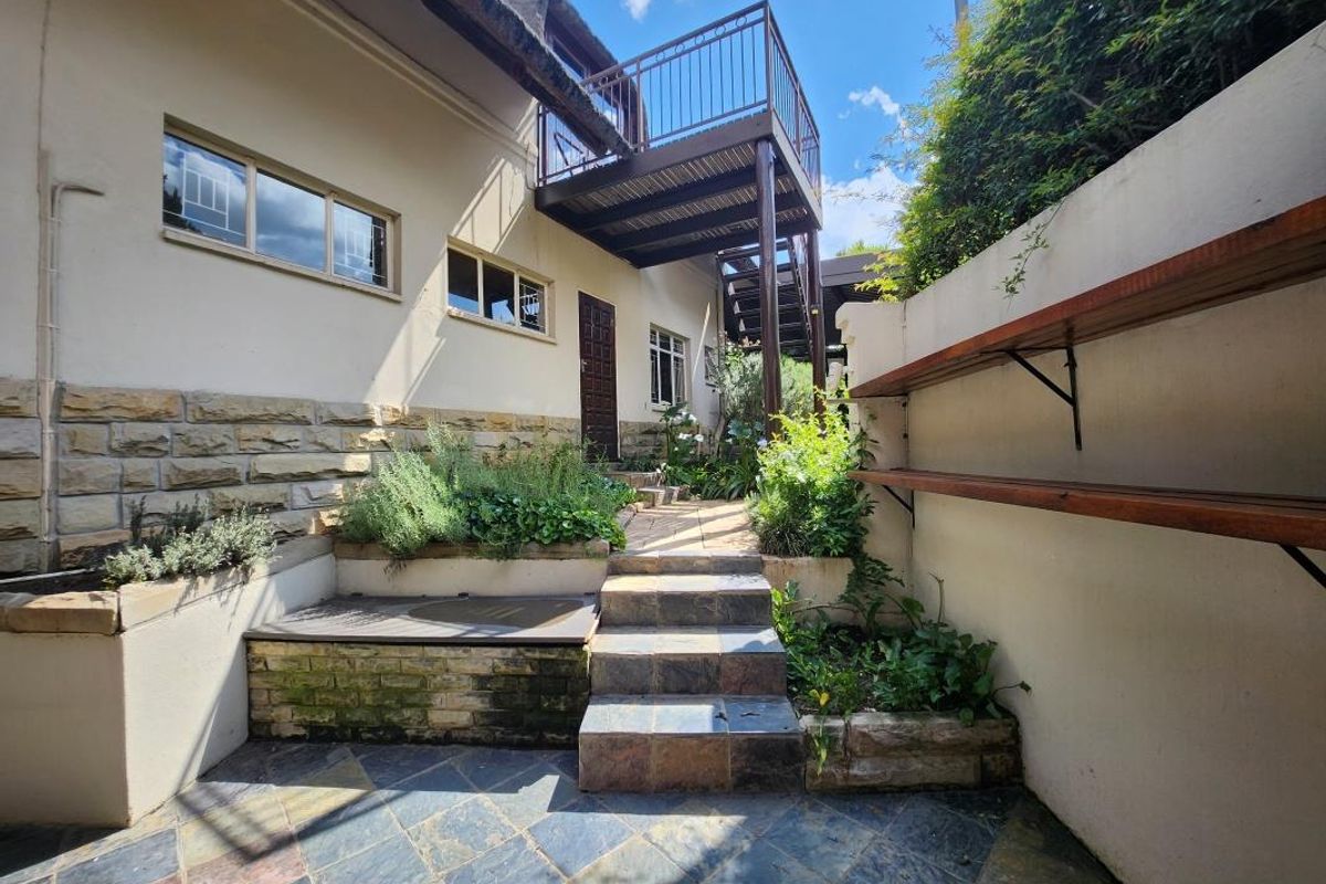 Rear courtyard area featuring slate paving, stone retaining walls, built-in shelving, and an external metal staircase leading to an upper balcony.