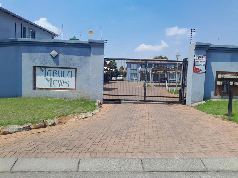 Front entrance view of Mabula Mews townhouse complex featuring a paved driveway, secure gated access, and perimeter wall with electric fencing.