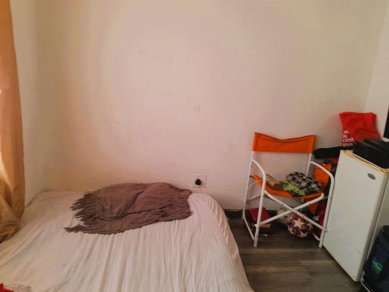 A compact bedroom featuring laminate flooring and a standard electrical outlet, providing a functional space for a single bed.