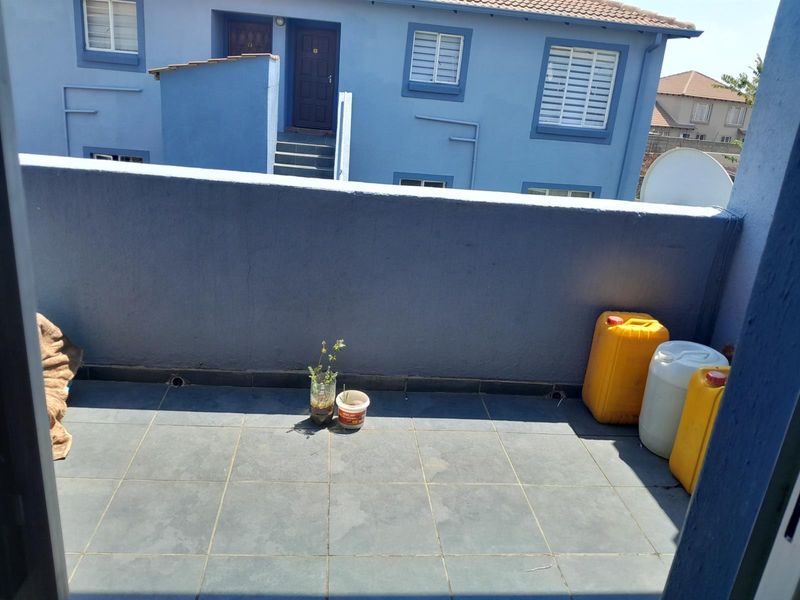 A functional balcony area featuring tiled flooring and a solid parapet wall, providing an outdoor space overlooking the townhouse complex.
