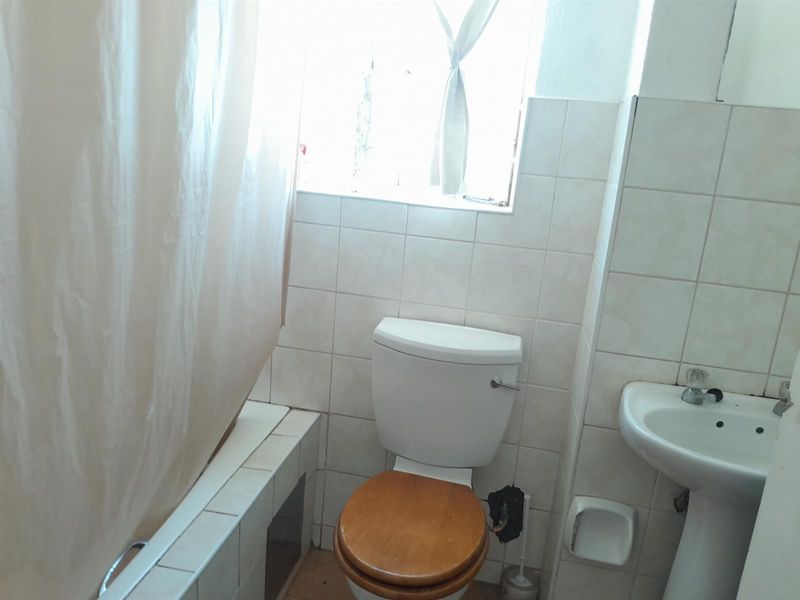 A compact bathroom featuring a bathtub, pedestal basin, and toilet with dated ceramic wall tiling and standard fixtures.