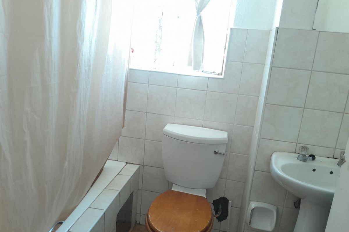 A compact bathroom featuring a bathtub, pedestal basin, and toilet with dated ceramic wall tiling and standard fixtures.