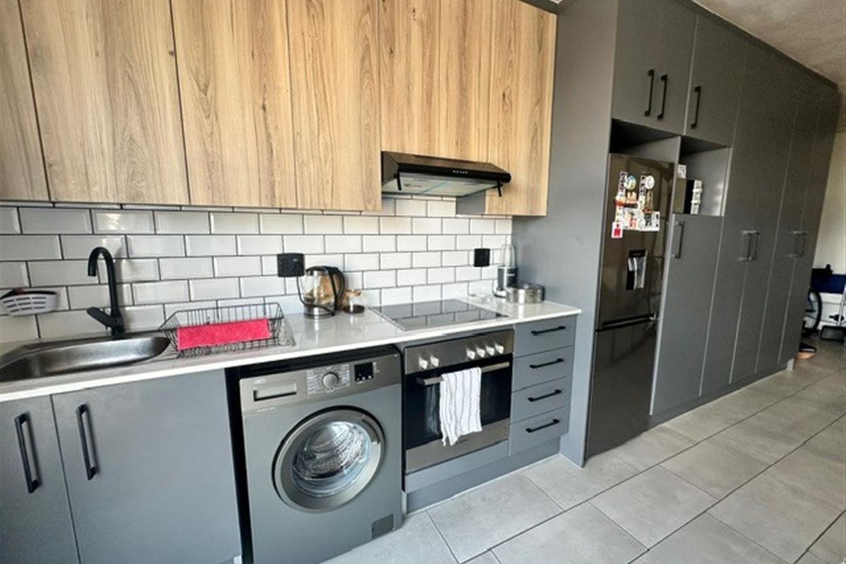 Modern kitchen featuring two-tone cabinetry, subway tile backsplash, integrated oven, hob, extractor fan, and dedicated space for a washing machine.