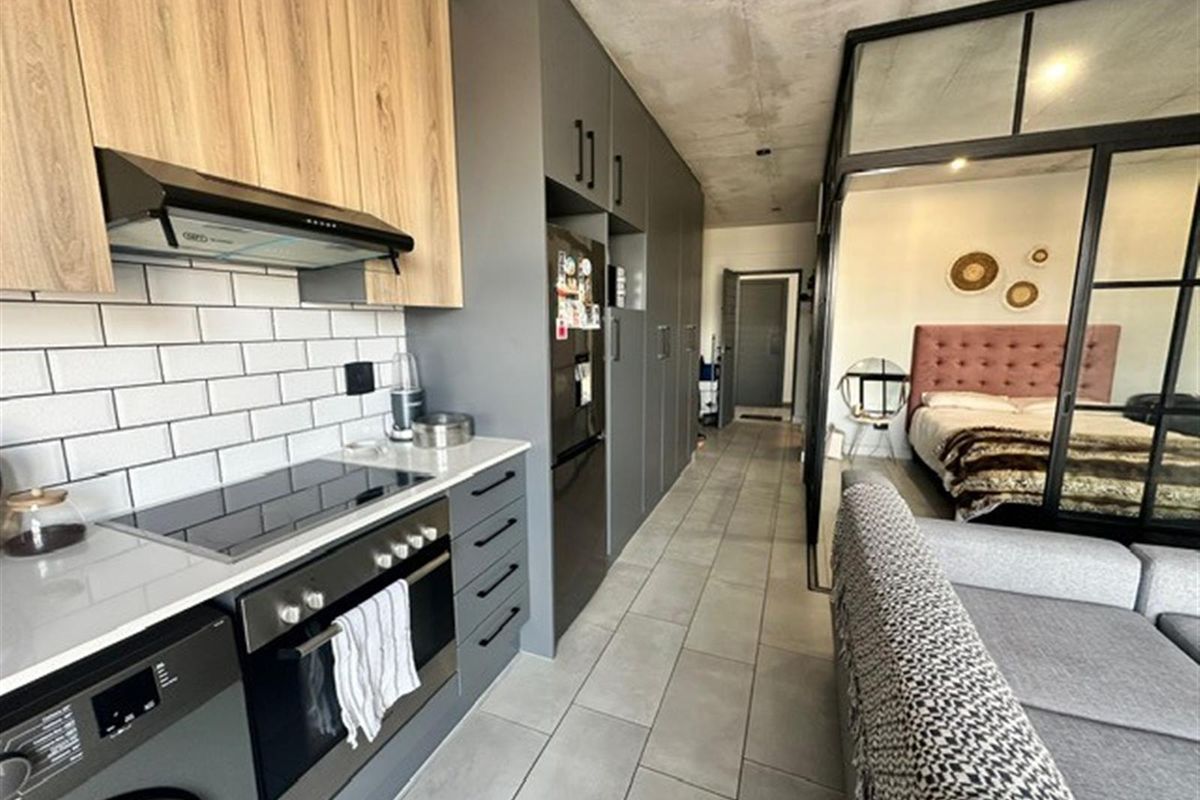 Modern open-plan apartment featuring a sleek kitchen with built-in cabinetry, integrated appliances, and a seamless transition to the bedroom area with industrial-style glass partitioning.