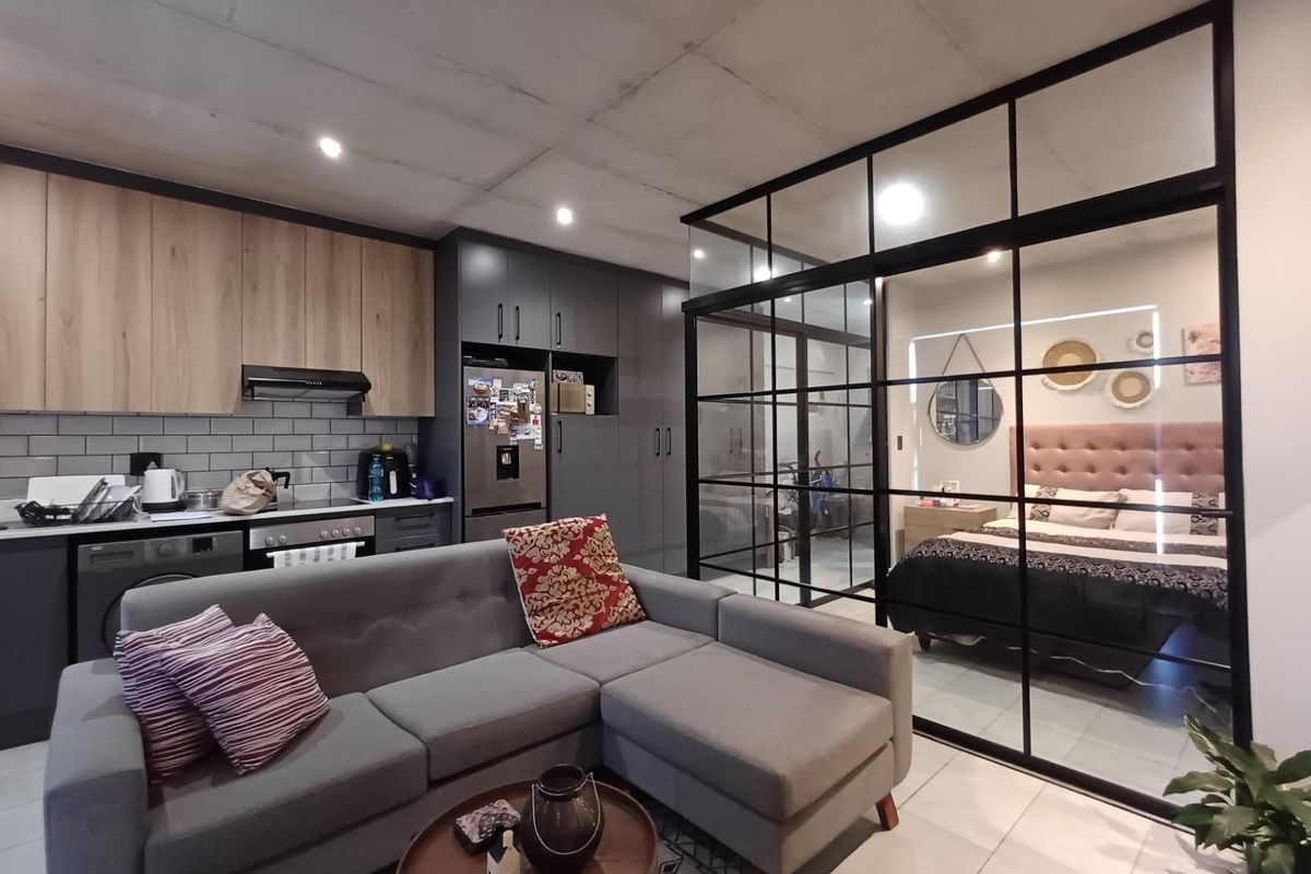 Modern open-plan apartment featuring a contemporary kitchen with sleek cabinetry, subway tile backsplash, and a stylish industrial-style glass partition separating the bedroom.
