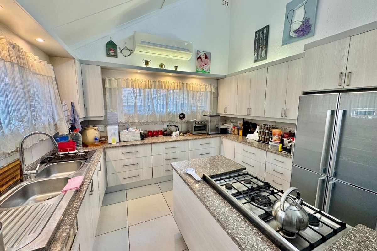 A well-appointed kitchen featuring light-toned cabinetry, granite countertops, a central island with a built-in gas hob, and high vaulted ceilings.