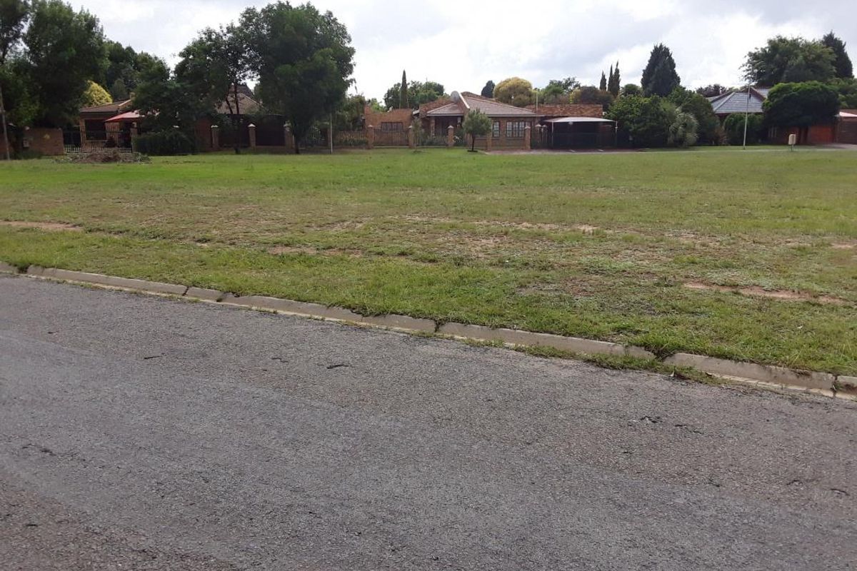 A street-level view of a vacant residential plot featuring an asphalt road, concrete curbing, and a grass verge.