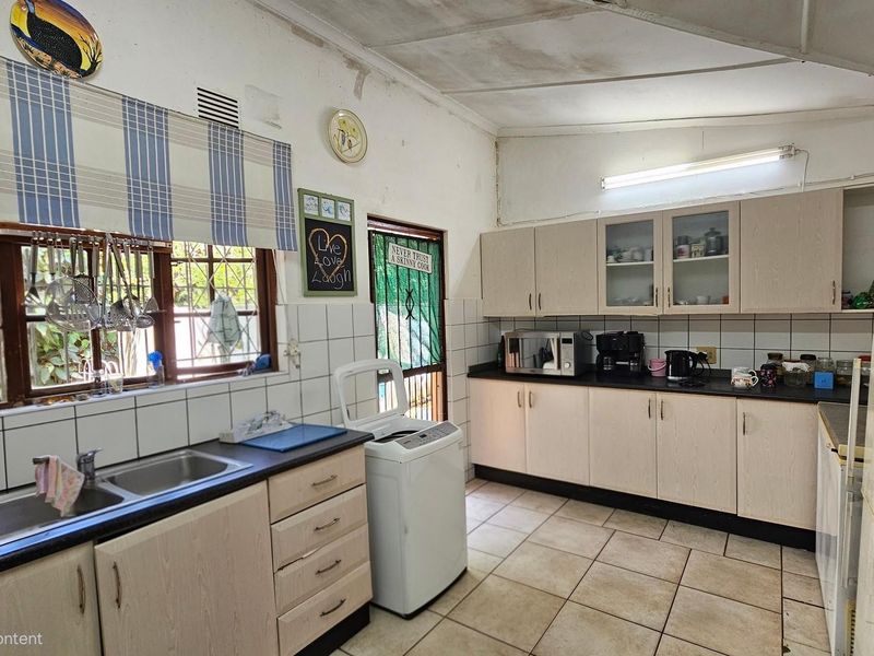 A functional kitchen featuring laminate cabinetry, double basin sink, tiled splashbacks, and tiled flooring, with visible signs of wear on the ceiling and cabinets.