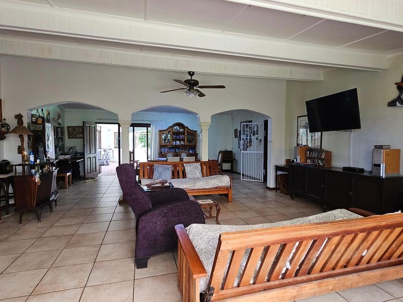Spacious open-plan living area featuring tiled flooring, exposed beam ceilings, and arched architectural details connecting to adjacent spaces.